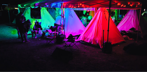 Colorful tents illuminated with neon lights at a nighttime event.