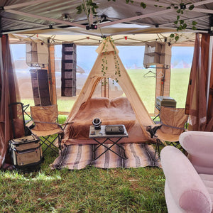 Camping setup with a teepee, chairs, and outdoor furniture under a canopy.